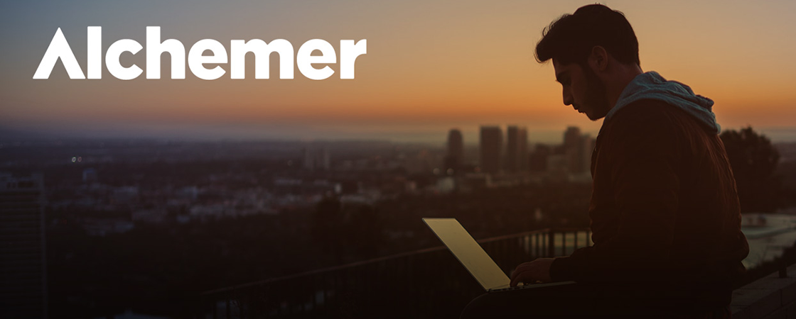 A person using a laptop outdoors at sunset with a city skyline in the background. The word Alchemer is displayed in white at the top left of the image.