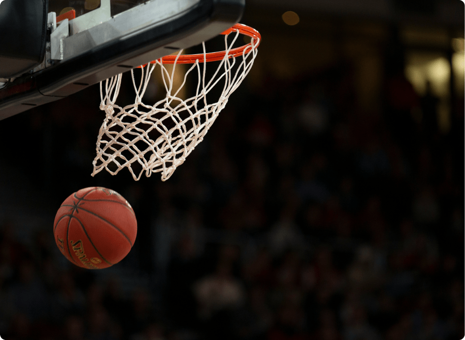 A basketball mid-air approaches the hoop, echoing the precision and excitement found in the software industry. The blurred audience in the dimly lit arena heightens the anticipation of a scoring play, much like fans eagerly watching their favorite teams on platforms like FanDuel.