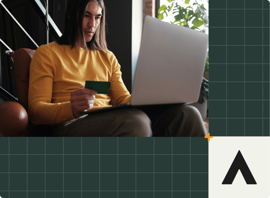 A person with long hair wearing a yellow sweater is seated indoors, engrossed in their laptop. They hold a green card, possibly related to the financial services industry, against a grid-patterned background with a logo featuring a black triangle on the bottom right.